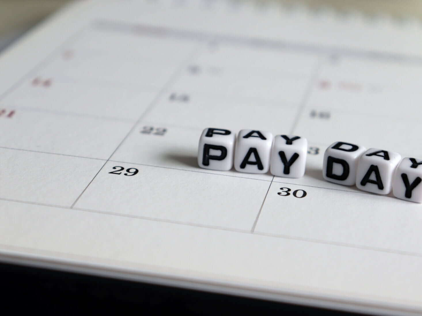 Un calendrier avec un dé orthographiant « PAY DAY » reposant sur le 29 et le 30.